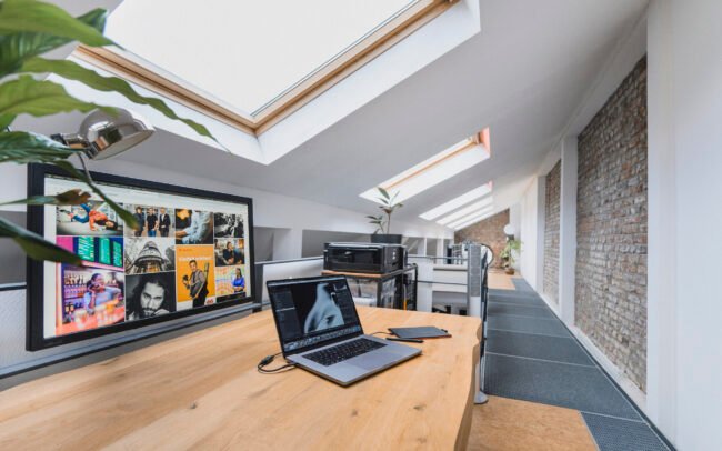 Moderner Arbeitsplatz mit Laptop und großem Monitor, der eine visuelle Webdesign-Referenz in einer Kölner Agenturumgebung zeigt.